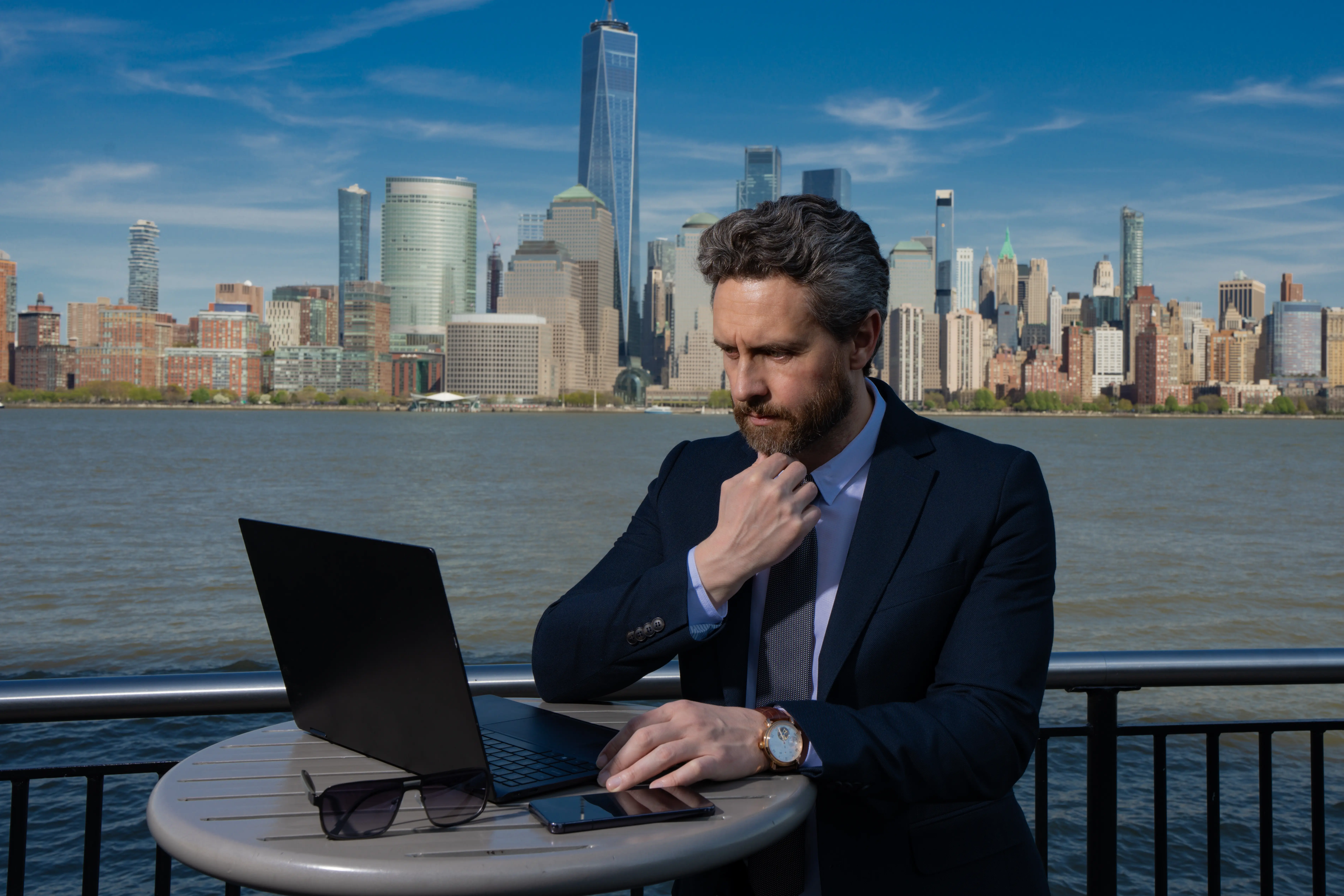 Photo of a mature American businessman using a laptop outdoors in New York, working remotely and signifying business success.
