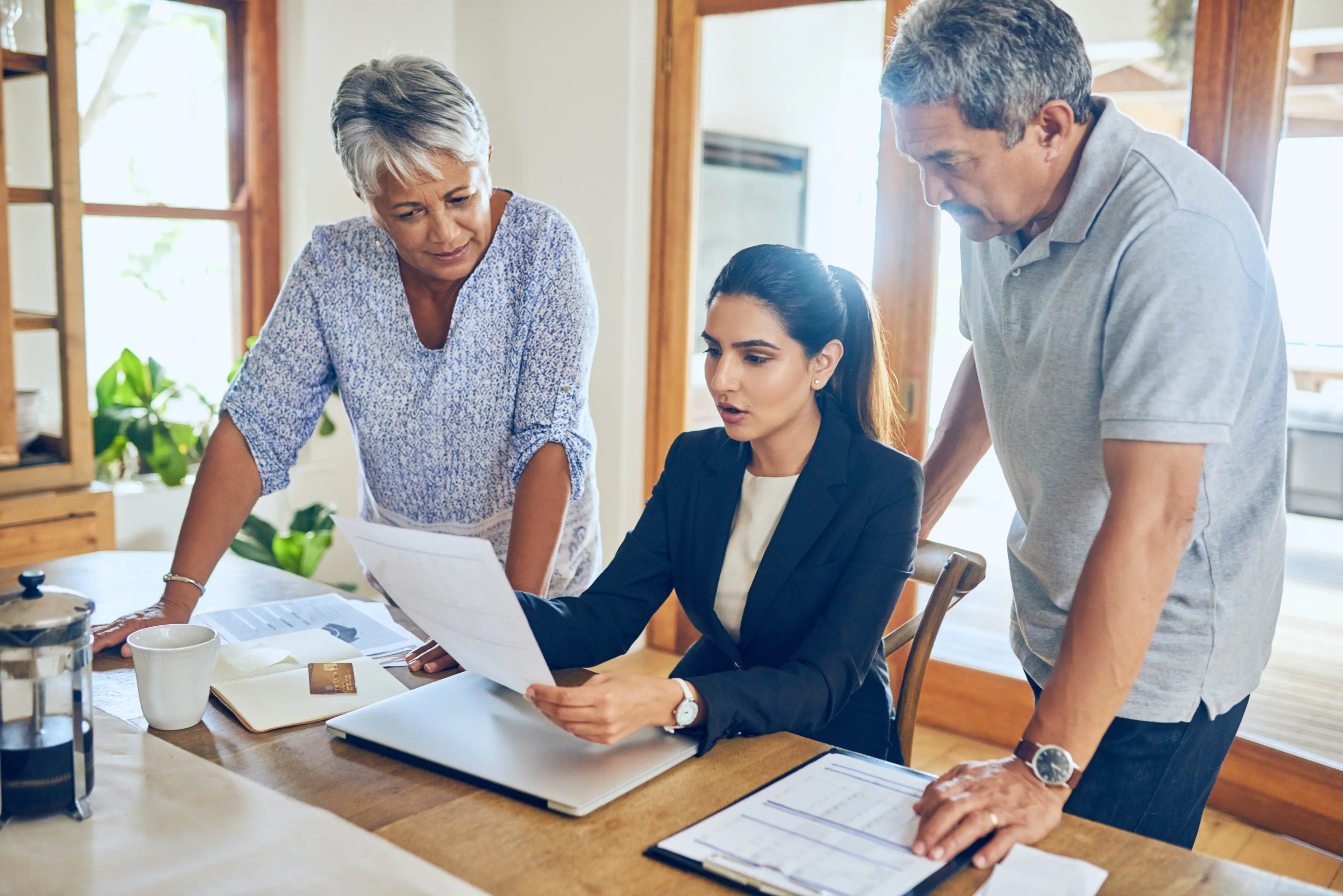 A financial consultant reviewing a budget with a senior couple, going over bills, paperwork, and life insurance documents; an elderly man and woman using a laptop with the advisor to plan retirement, pension payment, or investment.